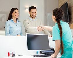 dental assistant shaking hands with male patient over front desk 