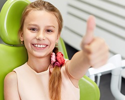 Young girl in dental chair giving thumbs up