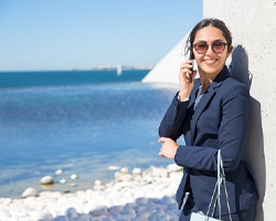 person standing on a beach, smiling, and talking on their phone