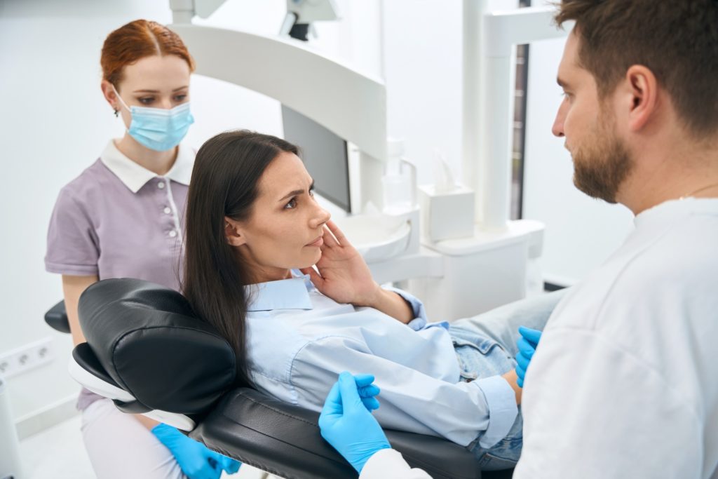 Concerned woman sitting in treatment chair while talking to dentist