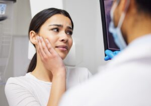 Patient holding face in pain while dentist sits nearby.